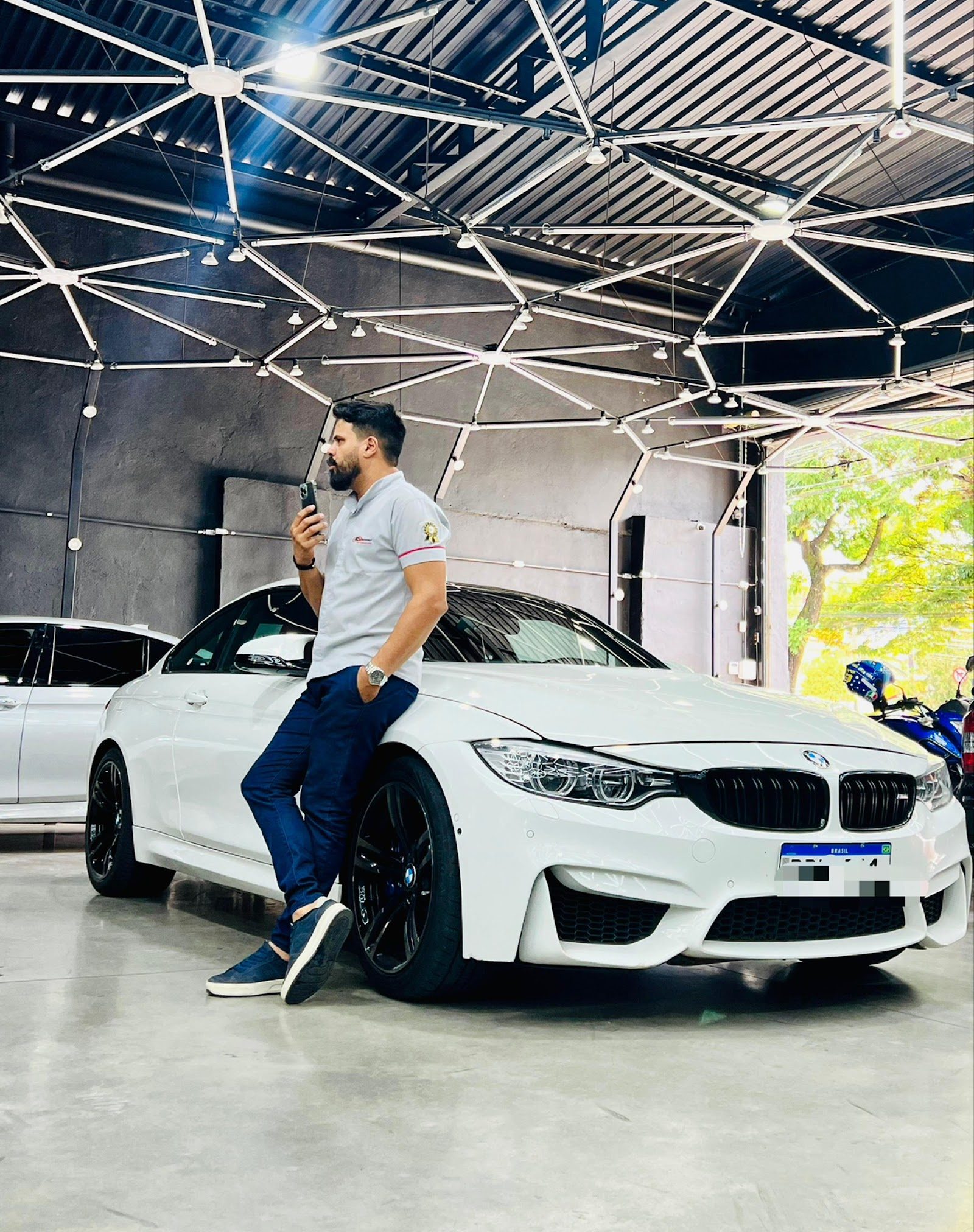 Robson no galpão de atendimento, encostado em um carro branco